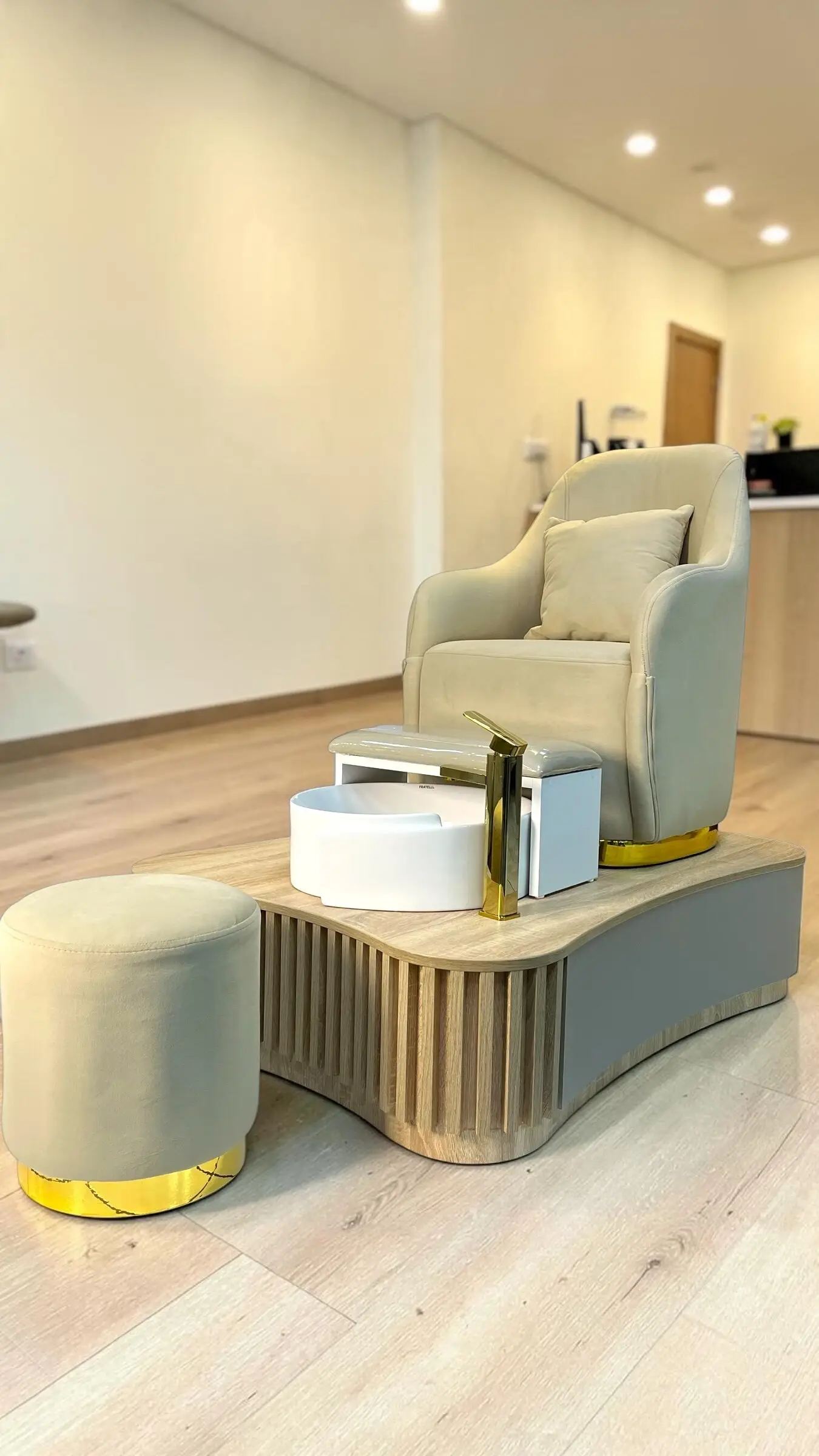 Estación de pedicure con sillón beige, poza blanca sobre tarima y puf