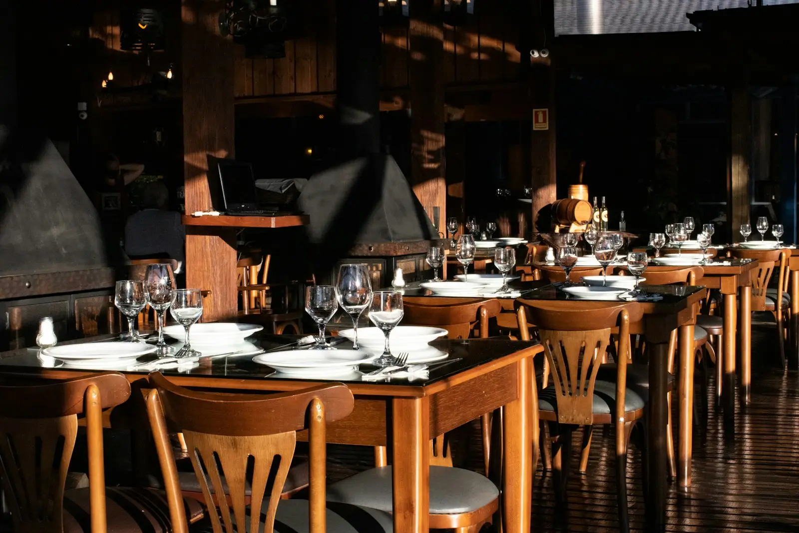 Restaurante con mesas y sillas de madera de respaldo calado, servidas con copas y platos
