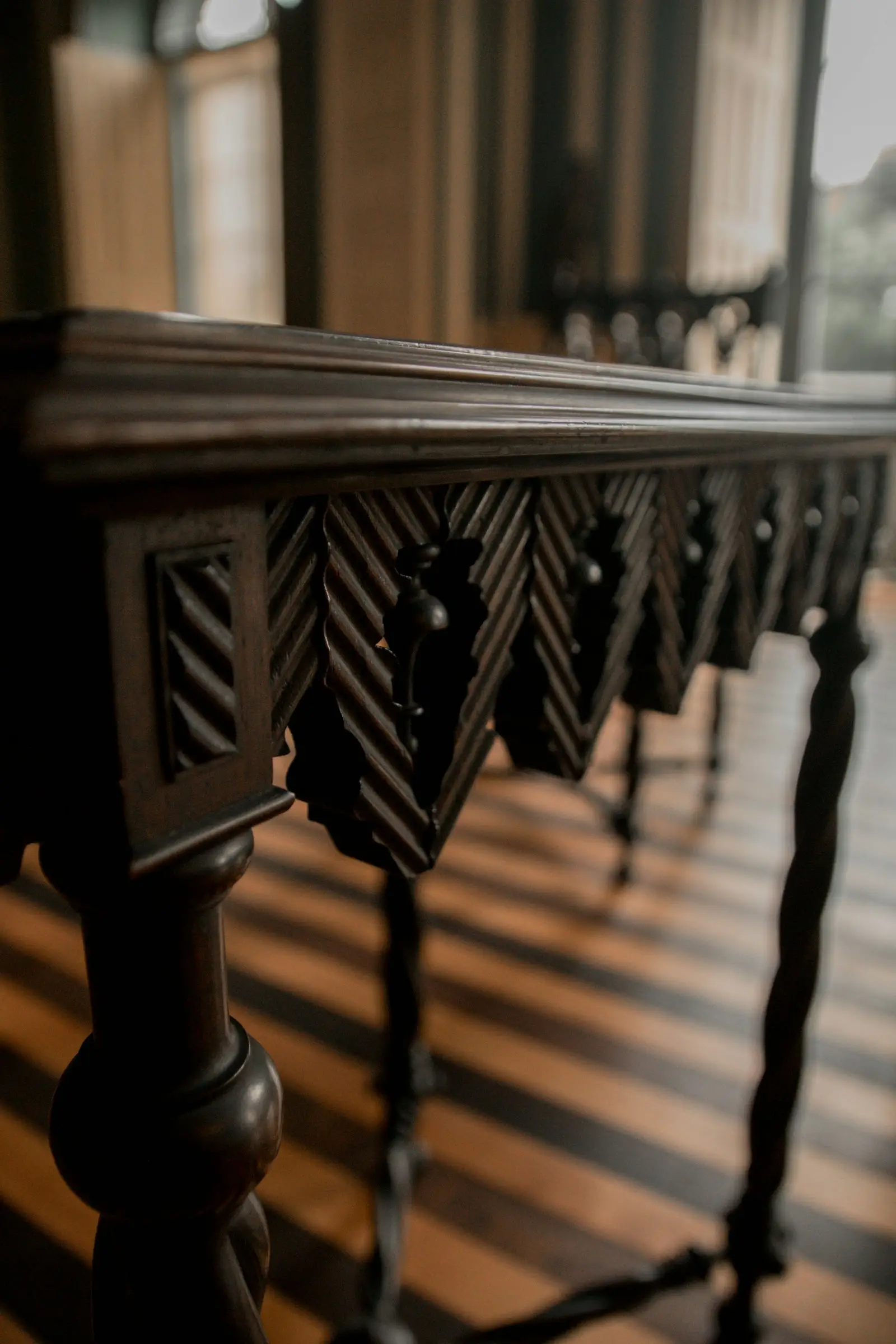 Detalle de mesa de madera oscura con faldón tallado y patas torneadas